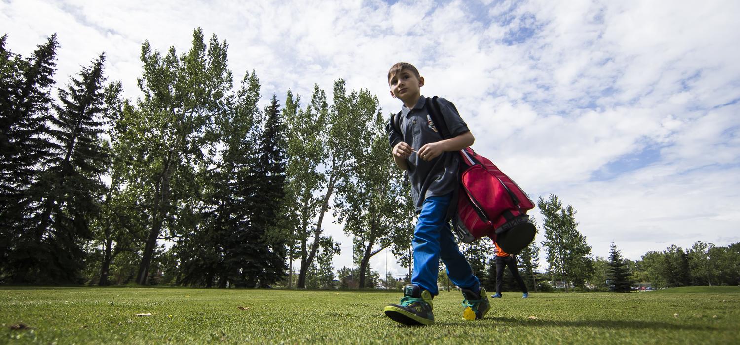 Summer camper walks across campus carrying a red golf bag