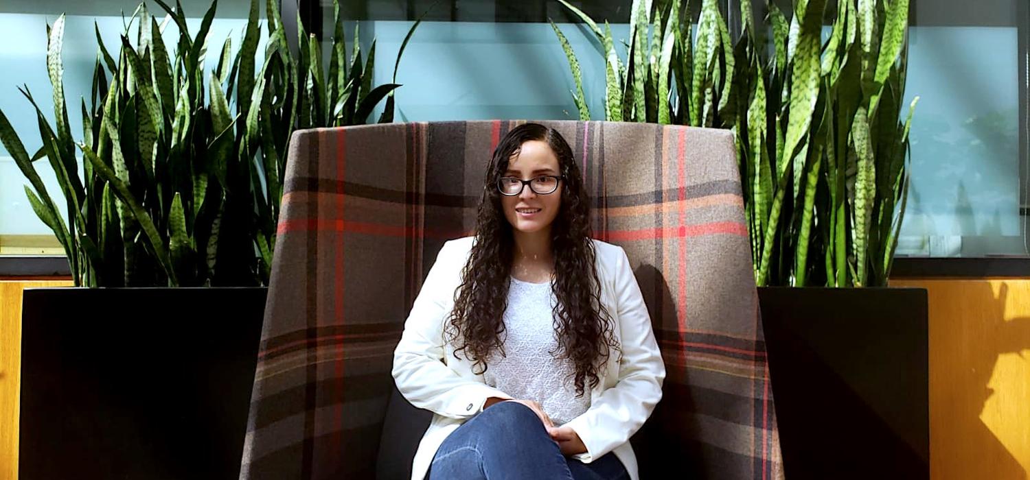 Student Valeria Marino sitting in a large chair with two large plants behind her