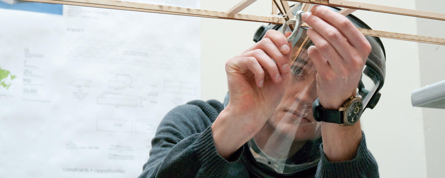 Male student working on an architectural model. He is focused.