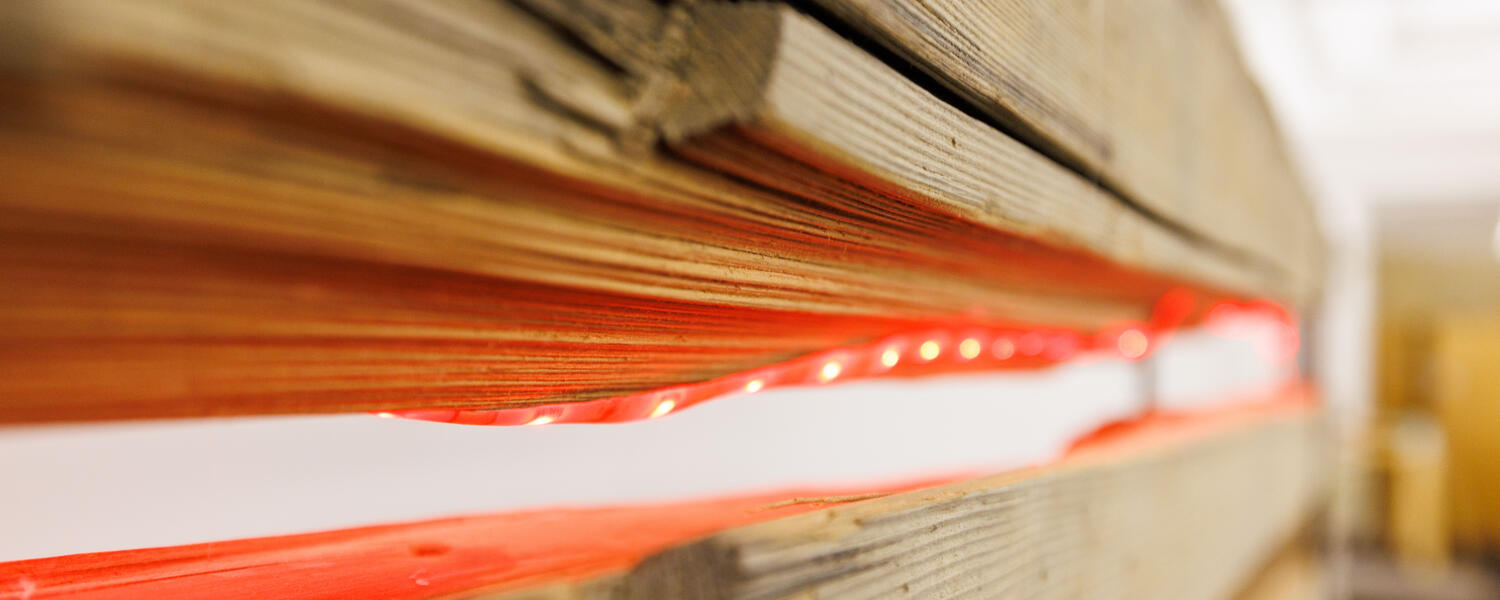 A close-up image of a piece of wood with an orange cable underneath it