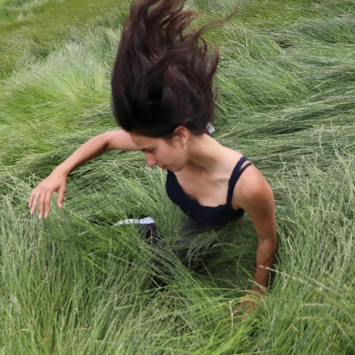 A person with long hair tumbling down a hill of tall grass.