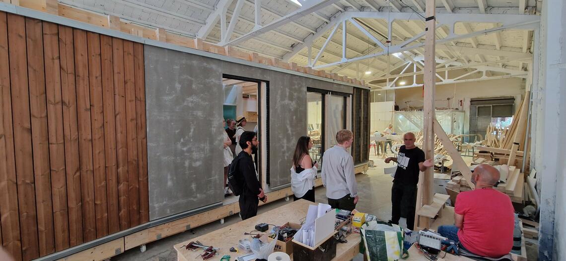 Architect David Juárez showing SAPL Barcelona students a stackable prefabricated dwelling under construction inside a warehouse. 