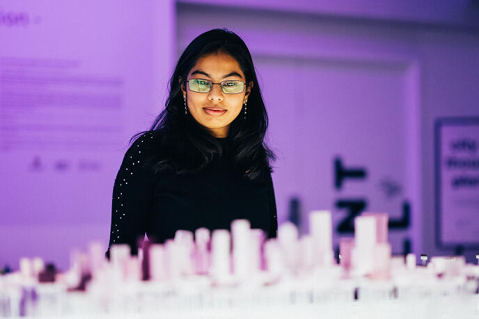 A person examines a large architectural model in a purple-lit gallery space.
