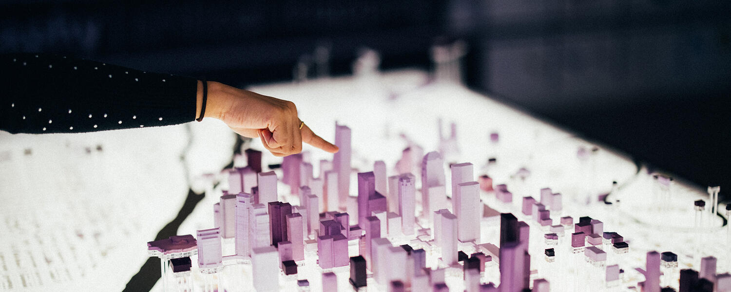 Close-up of hand pointing at a 3D model of the city with skyscrapers